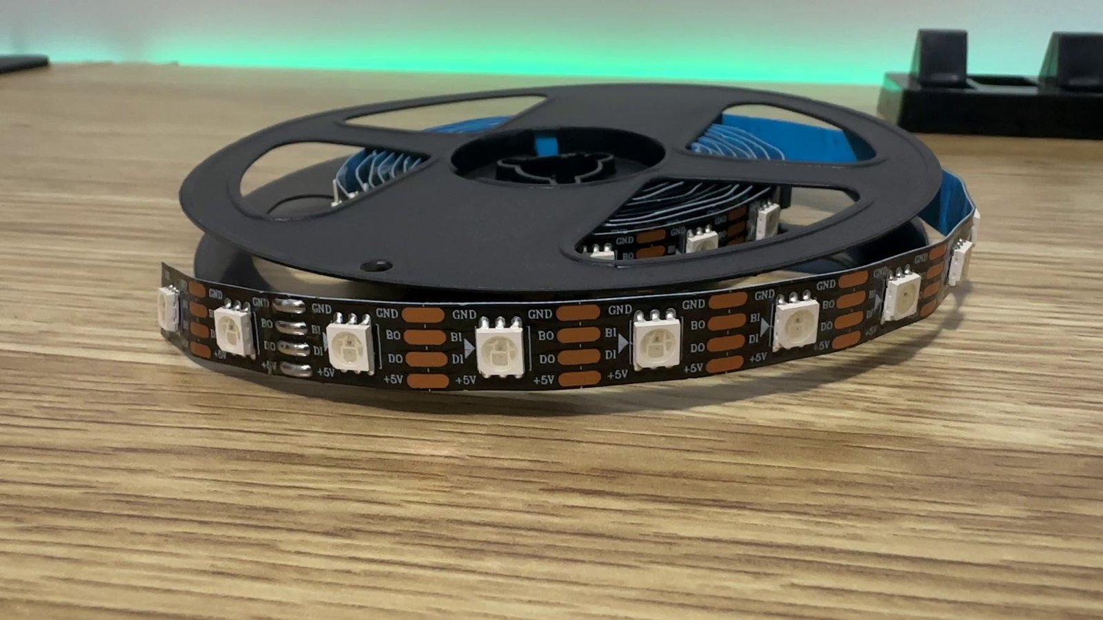 WS2813 LED Strip sitting on wooden work desk, green ambient lighting in the background, Smart LED Lighting